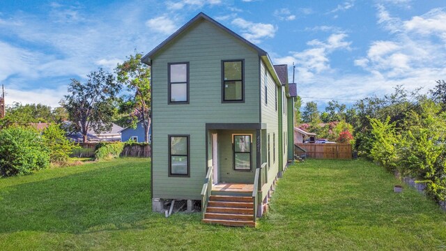rear view of house featuring a lawn and fence