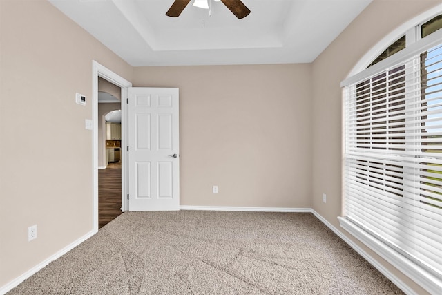 unfurnished bedroom with carpet, a ceiling fan, a tray ceiling, and baseboards
