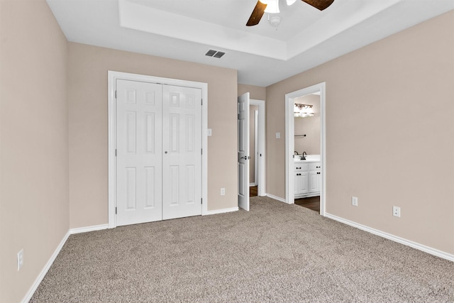 unfurnished bedroom with a closet, carpet, baseboards, visible vents, and a tray ceiling