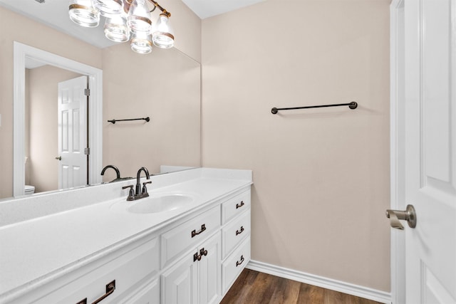 bathroom with an inviting chandelier, vanity, toilet, baseboards, and wood finished floors
