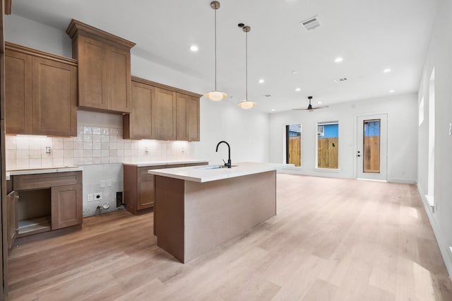 6703 Del Rio St, Houston, TX 77021 - kitchen featuring light wood-style floors, a kitchen island with sink, decorative backsplash, ceiling fan, and brown cabinets