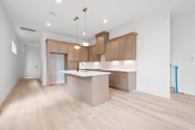 6703 Del Rio St, Houston, TX 77021 - kitchen featuring light wood-type flooring, decorative backsplash, a kitchen island with sink, pendant lighting, and light countertops