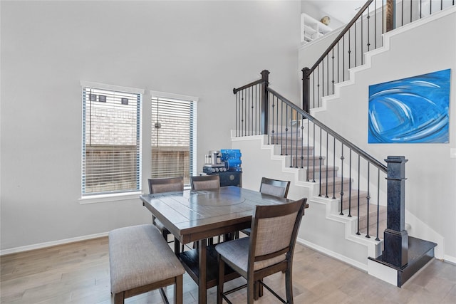 dining space with a high ceiling, stairs, light wood finished floors, and baseboards