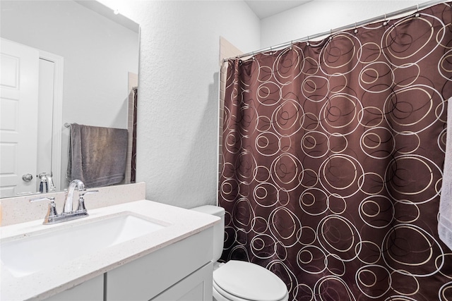 full bathroom featuring a textured wall, vanity, and toilet