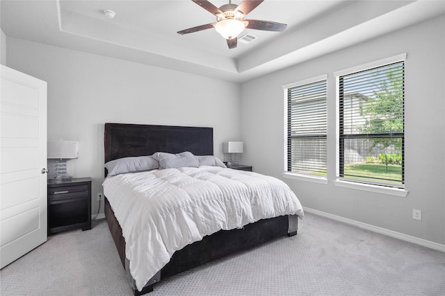 bedroom with a tray ceiling, visible vents, a ceiling fan, baseboards, and light colored carpet