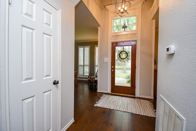 entrance foyer with a textured wall, visible vents, a notable chandelier, and dark wood-style floors