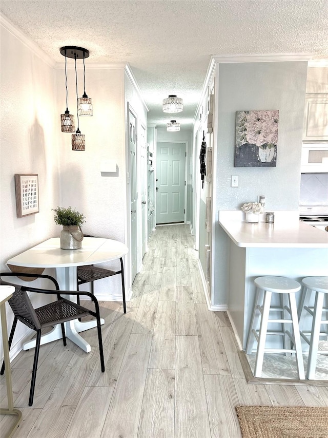 corridor featuring light wood finished floors, baseboards, a textured ceiling, and ornamental molding