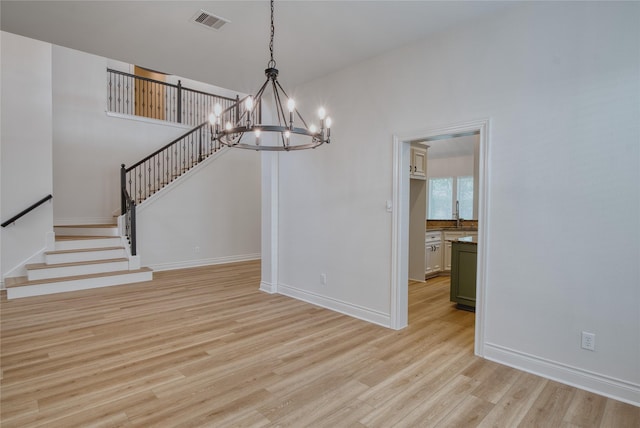 unfurnished dining area featuring visible vents, light wood-style floors, baseboards, a notable chandelier, and stairs