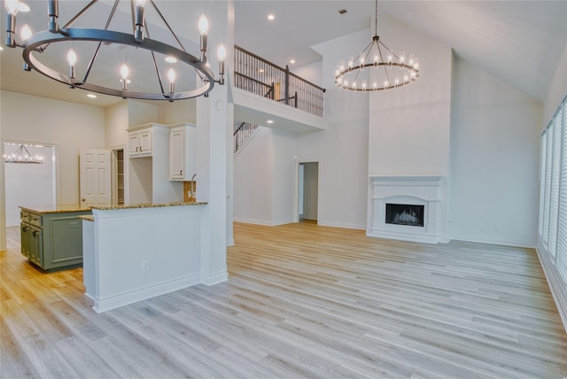 unfurnished living room featuring light wood finished floors, high vaulted ceiling, a chandelier, and baseboards