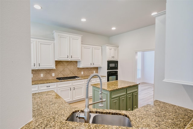 kitchen with decorative backsplash, green cabinetry, black appliances, a sink, and white cabinetry