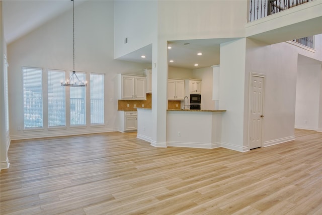 unfurnished living room with light wood-style floors, baseboards, a notable chandelier, and a high ceiling