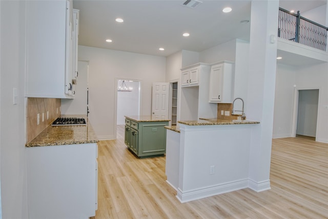 kitchen with green cabinetry, white cabinets, light wood finished floors, and light stone counters
