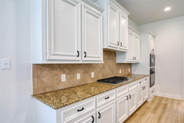 kitchen with light stone countertops, stainless steel gas stovetop, black oven, white cabinets, and built in microwave