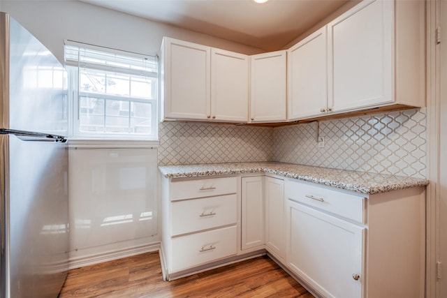 kitchen featuring light wood finished floors, decorative backsplash, freestanding refrigerator, and white cabinetry