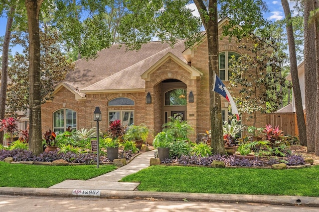 view of front of home with fence, roof with shingles, a front yard, and brick siding