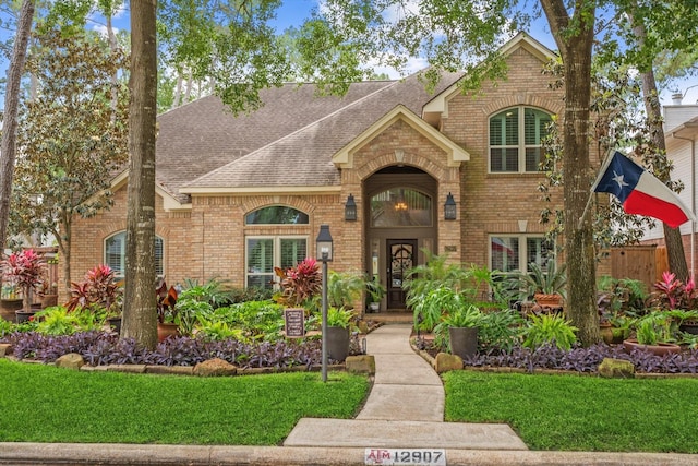 view of front of house featuring brick siding, fence, a front lawn, and roof with shingles