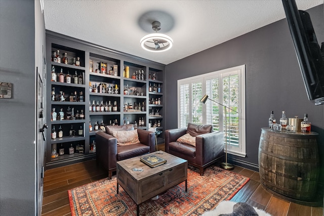 living area with wood finished floors, a bar, and a textured ceiling