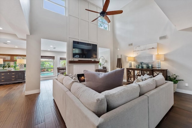living room featuring dark wood-type flooring, a ceiling fan, visible vents, baseboards, and a towering ceiling