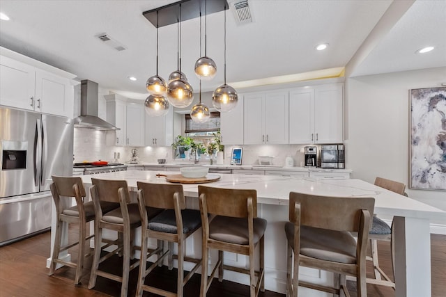 kitchen featuring tasteful backsplash, wall chimney exhaust hood, visible vents, a kitchen island, and appliances with stainless steel finishes