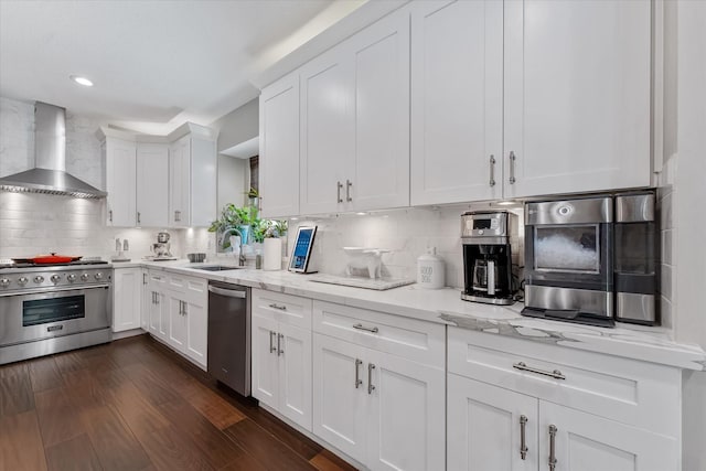 kitchen with tasteful backsplash, stainless steel appliances, a sink, white cabinetry, and wall chimney exhaust hood