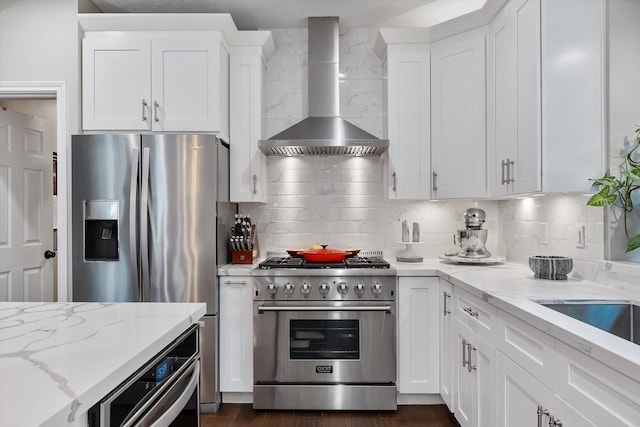 kitchen featuring light stone countertops, wall chimney exhaust hood, backsplash, white cabinets, and appliances with stainless steel finishes