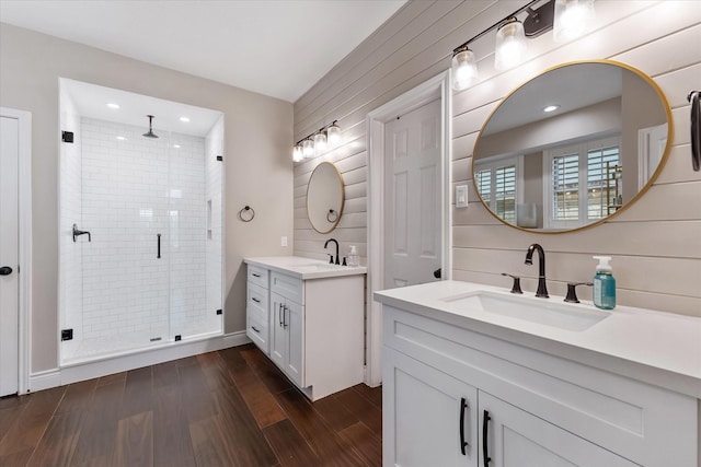 bathroom featuring a stall shower, two vanities, wood finished floors, and a sink