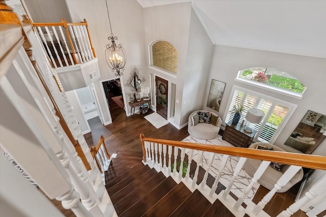 stairs with a high ceiling, a chandelier, crown molding, baseboards, and wood finished floors