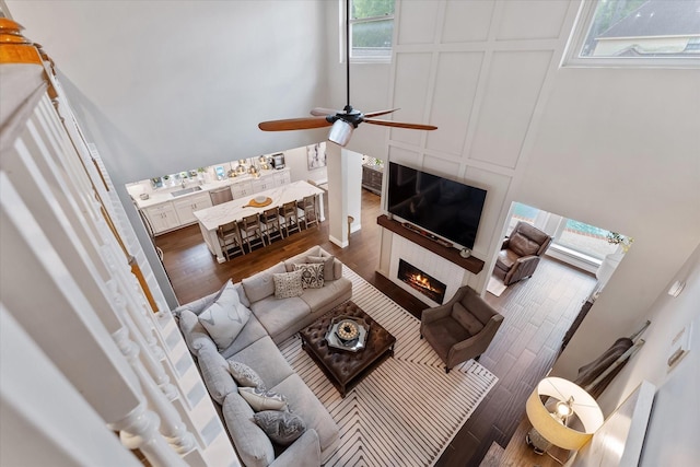 living room featuring wood finished floors, a ceiling fan, and a lit fireplace