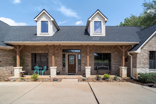 view of front facade featuring brick siding, roof with shingles, and covered porch