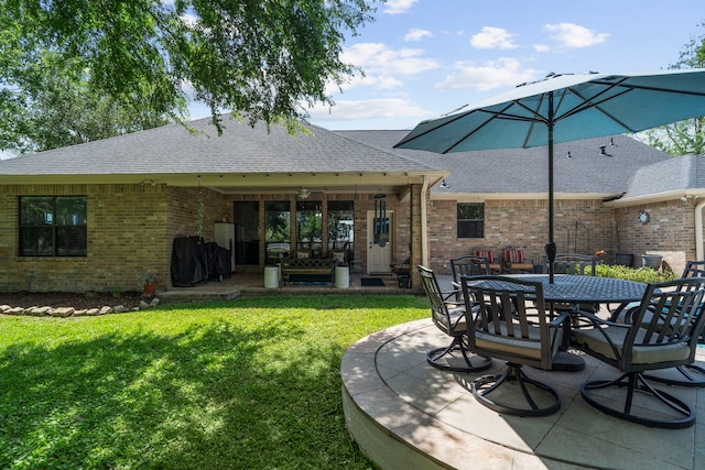 rear view of house with a ceiling fan, a shingled roof, a yard, a patio area, and brick siding