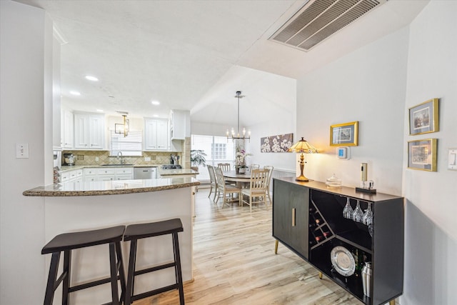 kitchen featuring a sink, light wood finished floors, backsplash, white cabinetry, and visible vents