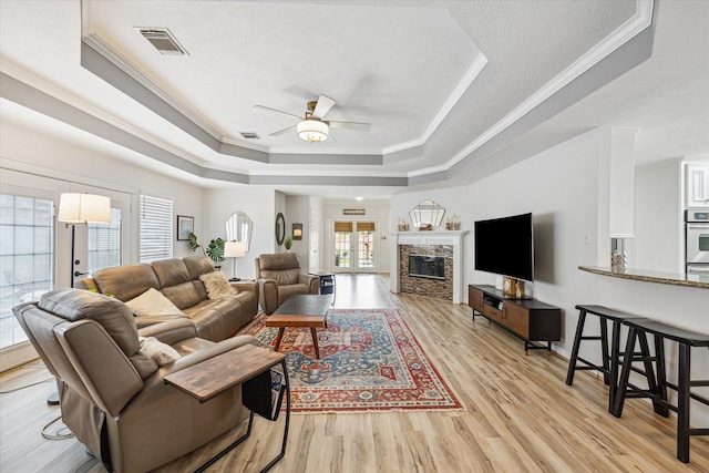 living area featuring a ceiling fan, light wood-style floors, a raised ceiling, ornamental molding, and visible vents