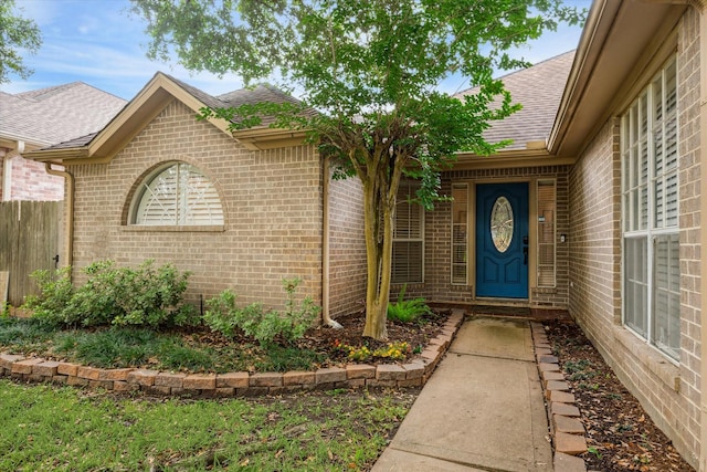 property entrance with fence, brick siding, and roof with shingles