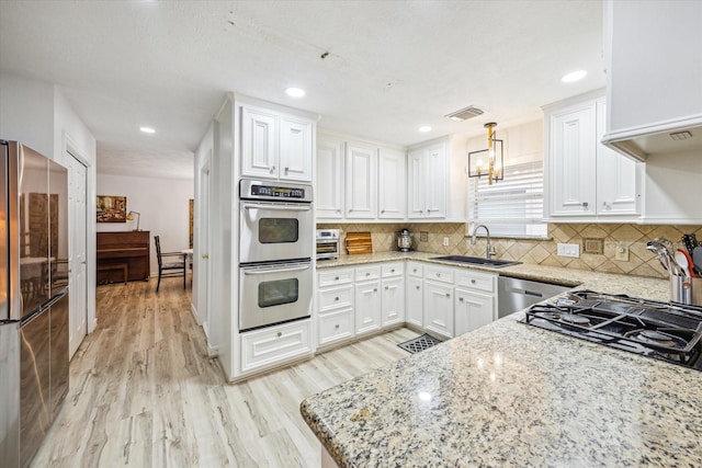 kitchen with a sink, light wood finished floors, white cabinets, appliances with stainless steel finishes, and visible vents
