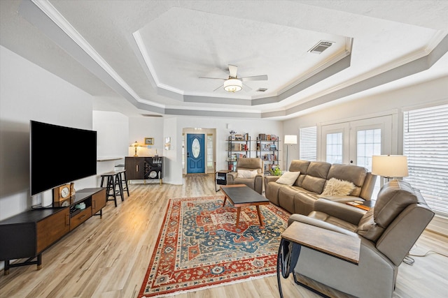 living room with light wood-style flooring, ornamental molding, and a raised ceiling
