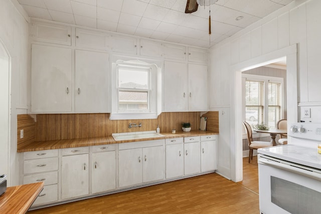 kitchen with white range with electric cooktop, tile counters, a sink, light wood-type flooring, and white cabinetry