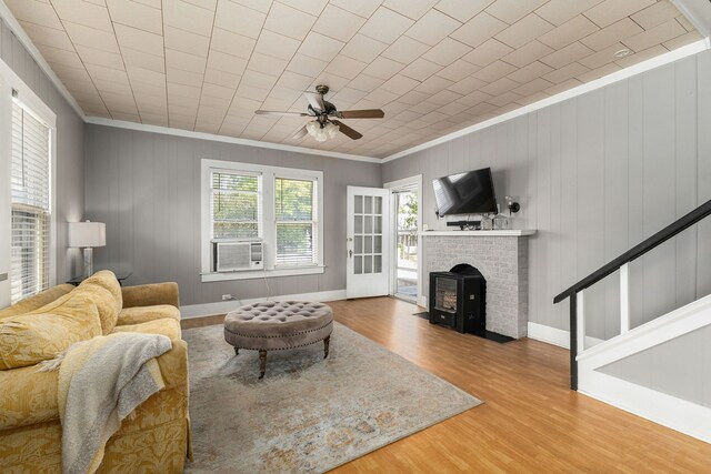 living room with baseboards, a brick fireplace, wood finished floors, ceiling fan, and ornamental molding