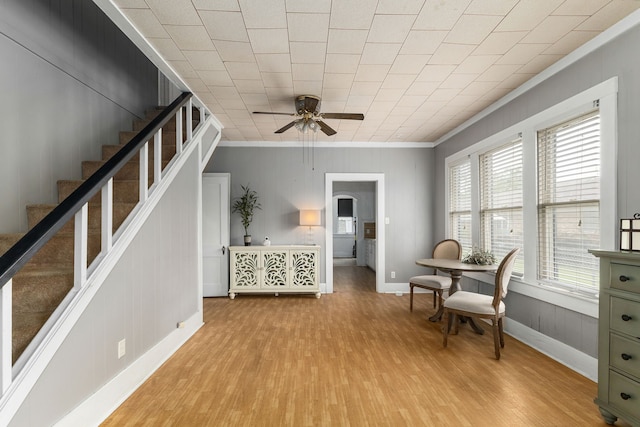 interior space with ceiling fan, baseboards, crown molding, and light wood-style flooring
