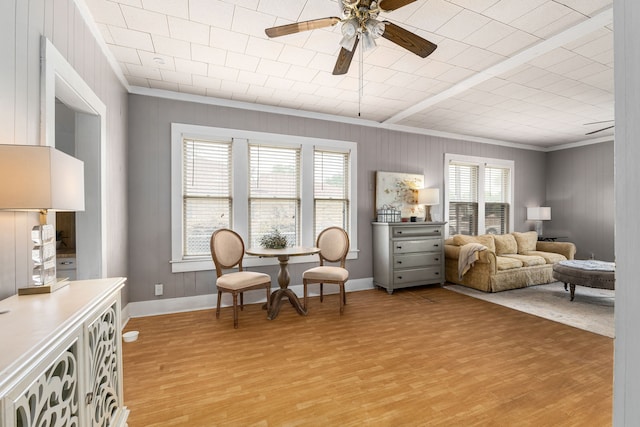 living area featuring light wood finished floors, wooden walls, ceiling fan, and crown molding