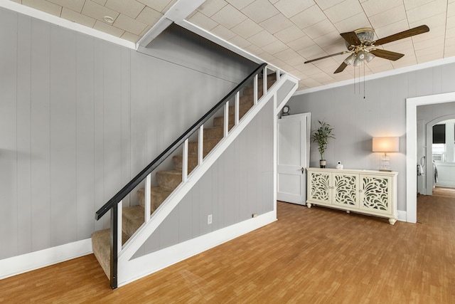 staircase with baseboards, a ceiling fan, wood finished floors, and arched walkways