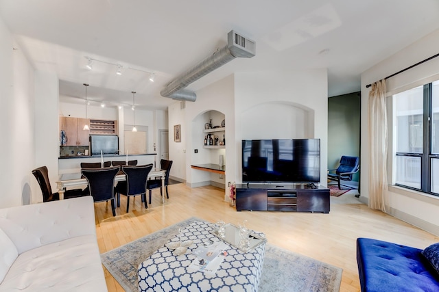 living area featuring light wood-style floors, rail lighting, and built in shelves