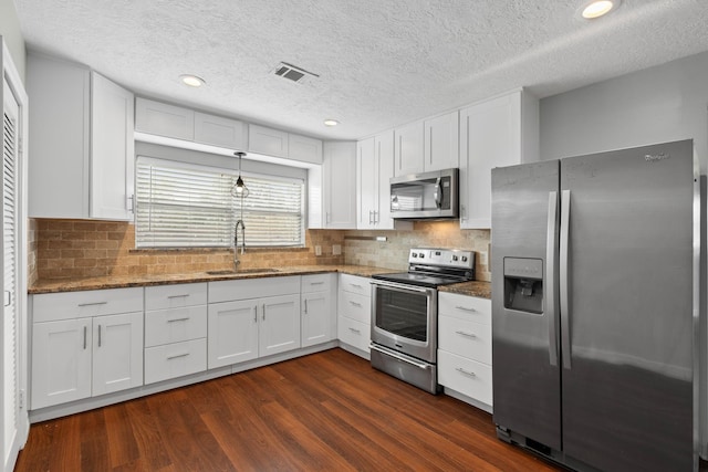 kitchen with white cabinetry, dark stone counters, stainless steel appliances, and a sink