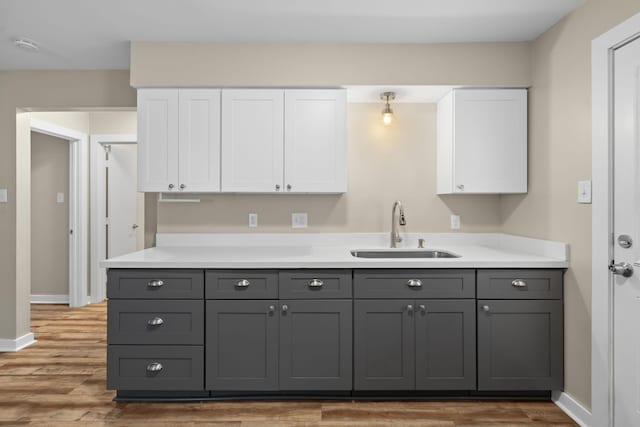 kitchen featuring white cabinets, wood finished floors, a sink, and gray cabinets