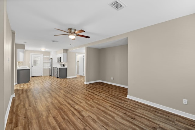 unfurnished living room featuring wood finished floors, visible vents, baseboards, and ceiling fan