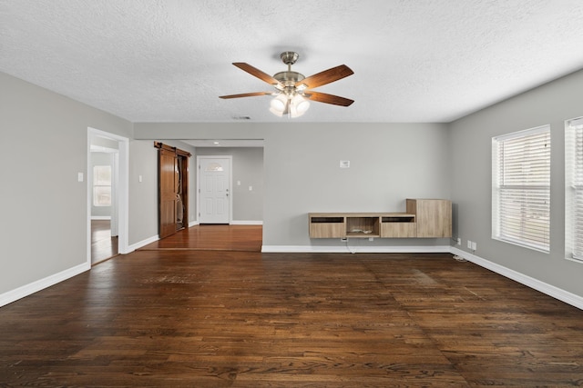 unfurnished room featuring a barn door, a textured ceiling, ceiling fan, baseboards, and dark wood-style floors
