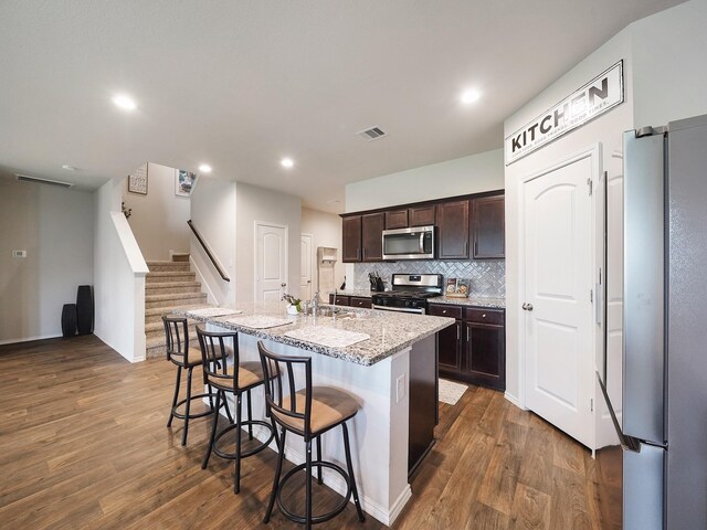 2423 Staverton Cir, Spring, TX 77373 - kitchen featuring a kitchen breakfast bar, an island with sink, dark brown cabinetry, stainless steel appliances, and dark wood-type flooring