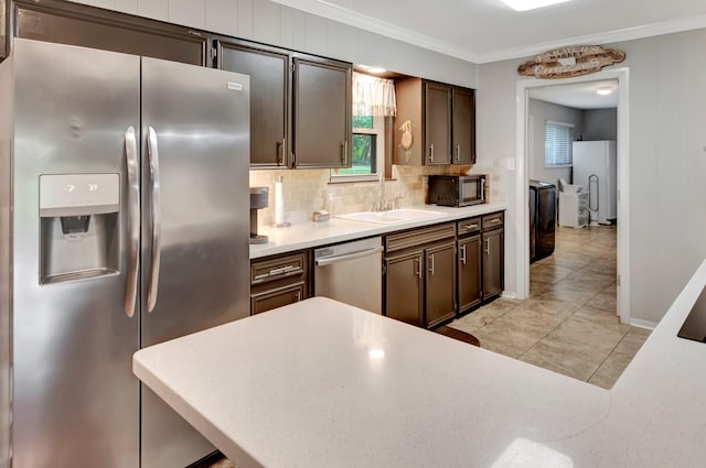 kitchen featuring washer and clothes dryer, a sink, crown molding, tasteful backsplash, and appliances with stainless steel finishes