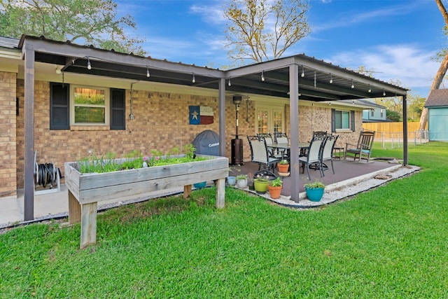 rear view of property featuring a lawn, fence, a garden, a patio, and brick siding