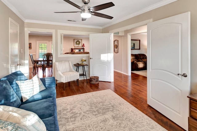 living room featuring a ceiling fan, visible vents, dark wood-type flooring, and crown molding