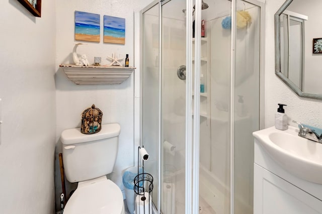 bathroom with toilet, a textured wall, vanity, and a stall shower